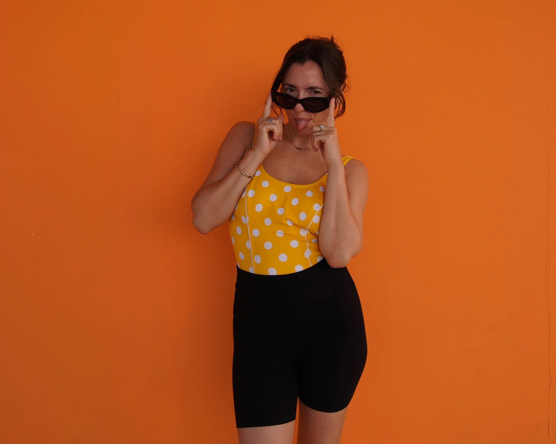 Amber vor einer orangenen Wand, mit Sonnenbrille und gelbem gepunktetem Oberteil